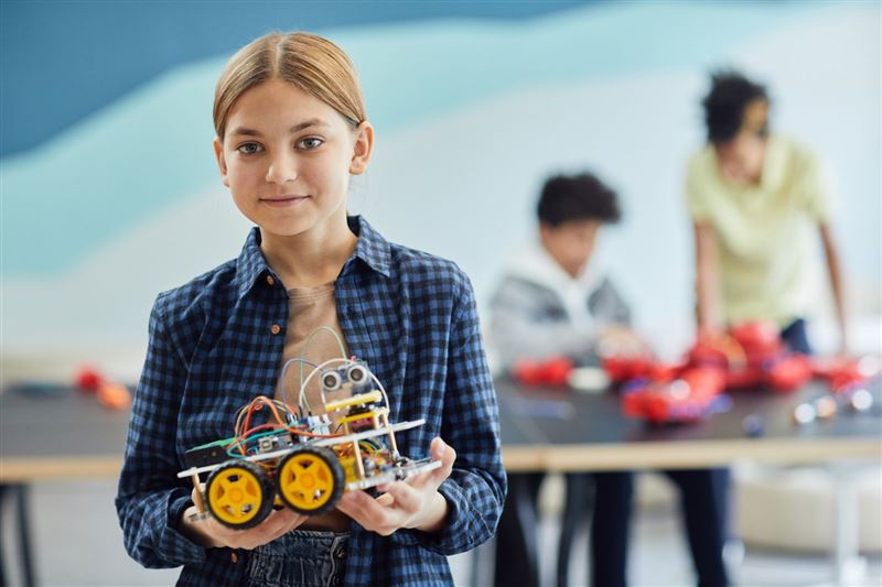 A girl holding a small robot with yellow wheels in both hands
