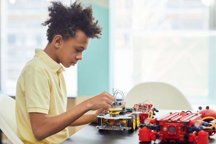 A boy in a yellow shirt assembling a small robot at a table