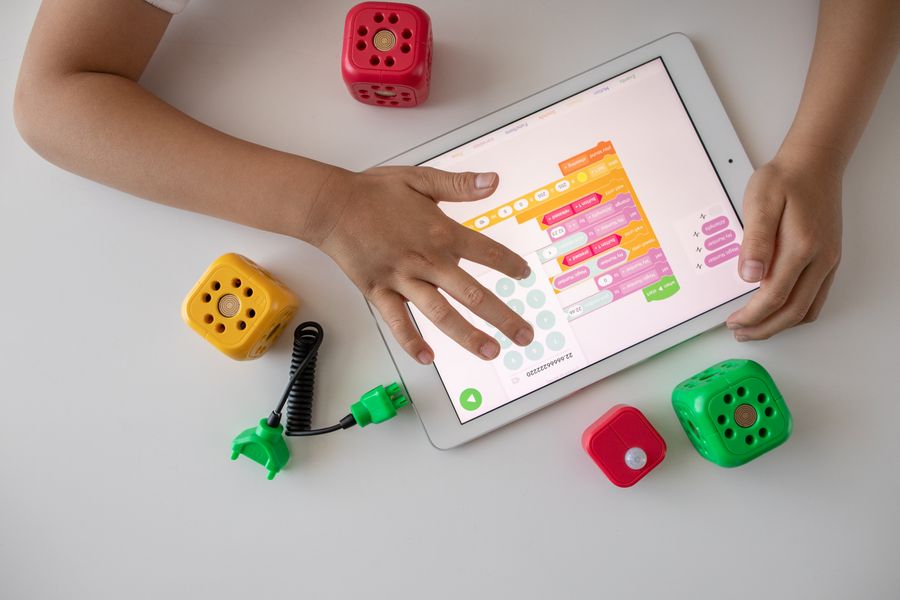 A child's hands using a tablet with a block coding app beside robot modules