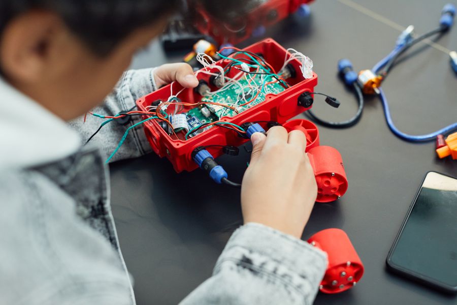 A boy connecting a wire to a robot with an exposed circuit board